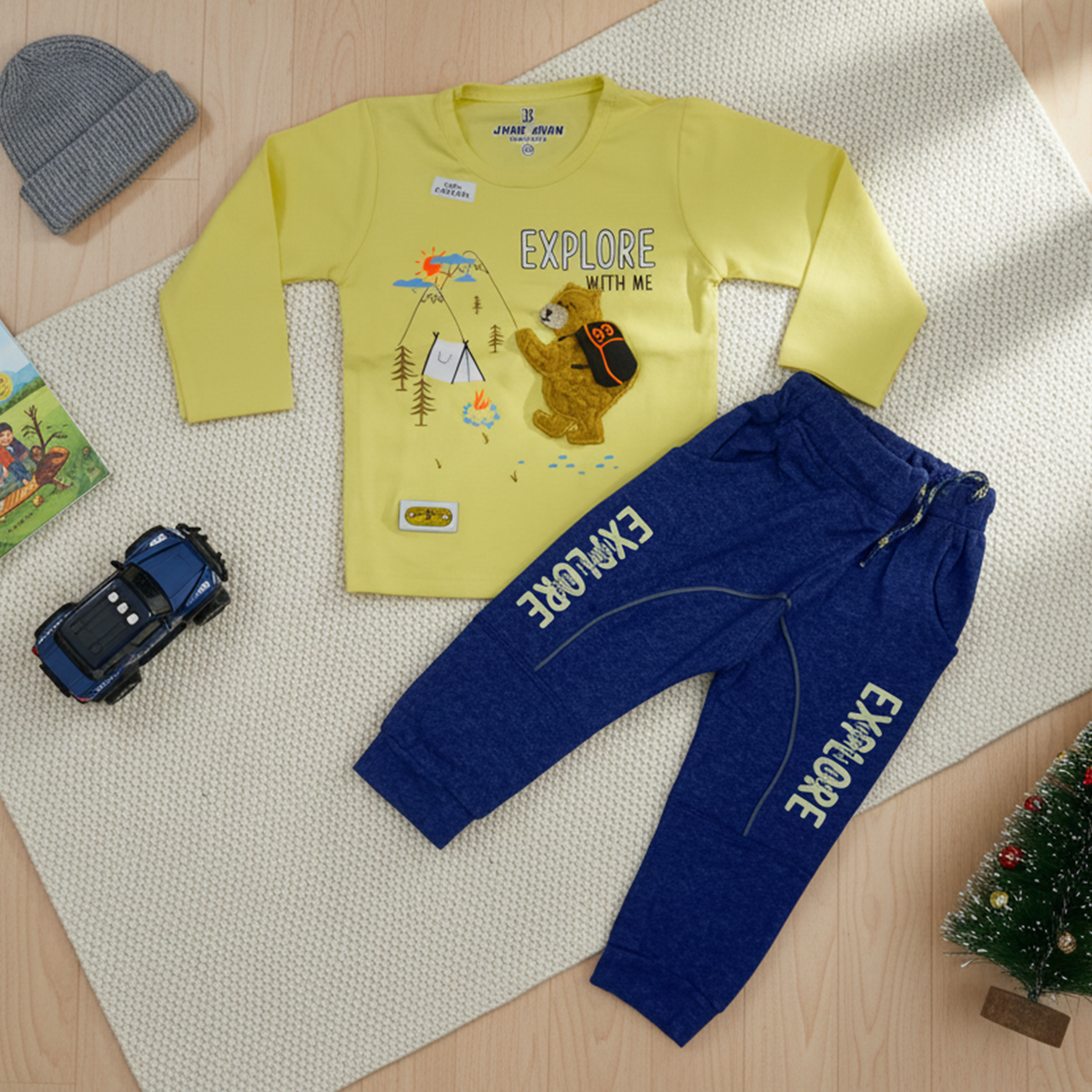 Child wearing a yellow long-sleeve shirt and blue pants with 'EXPLORE' text, standing in a bright room with a bookshelf.