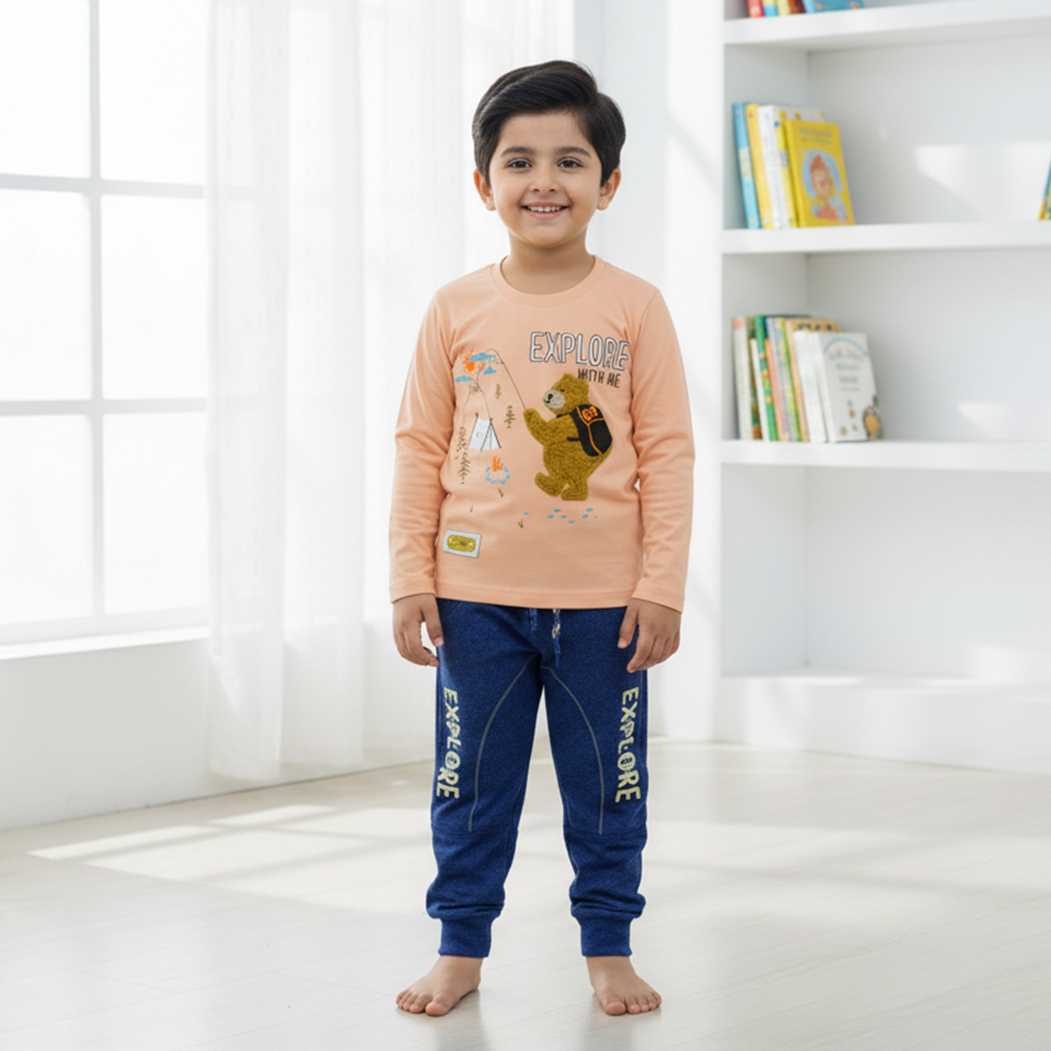 Child wearing a peach long-sleeve shirt and blue pants with 'EXPLORE' text, standing in a bright room.