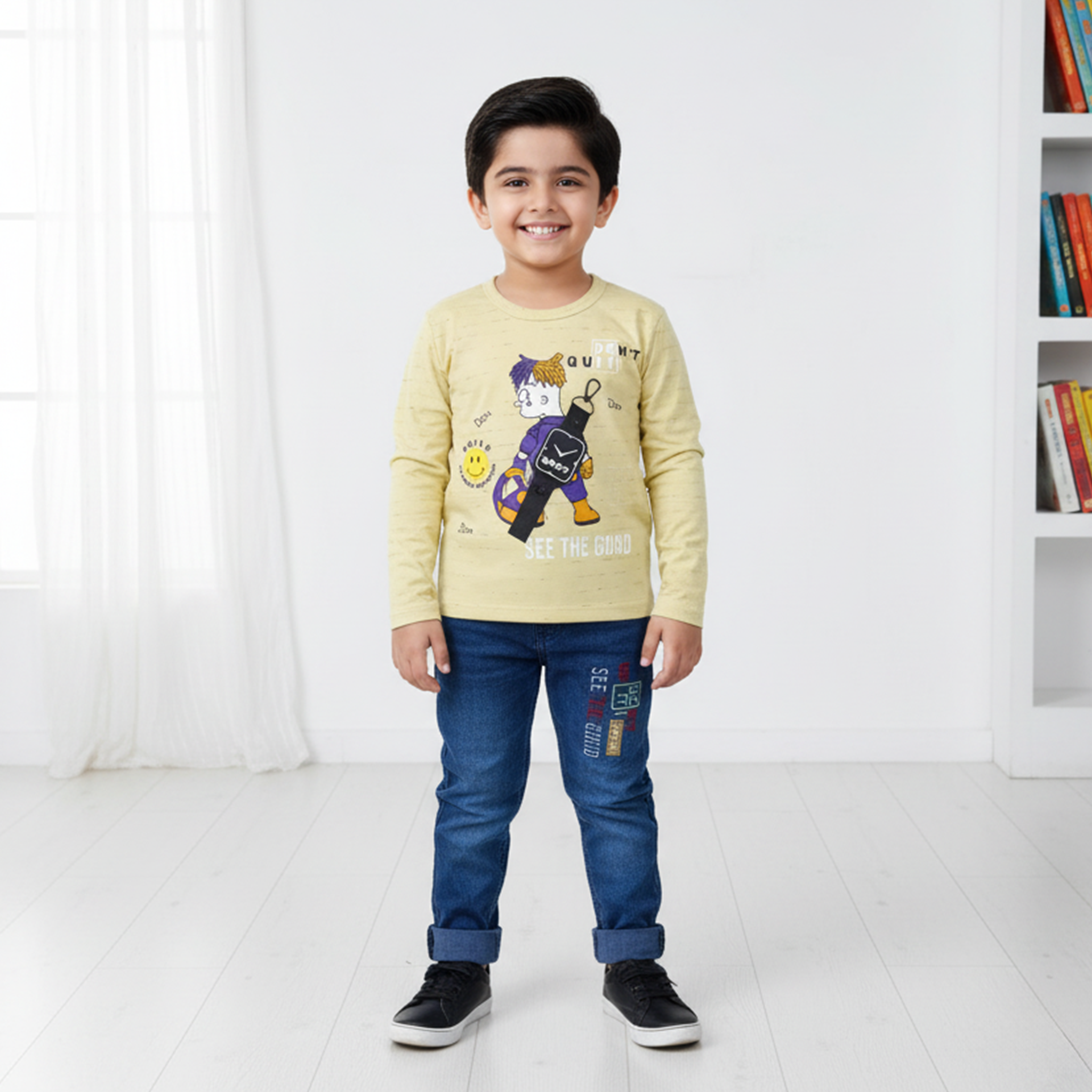 Child wearing a yellow sweater with a graphic design and blue jeans in a room with white walls and a bookshelf.